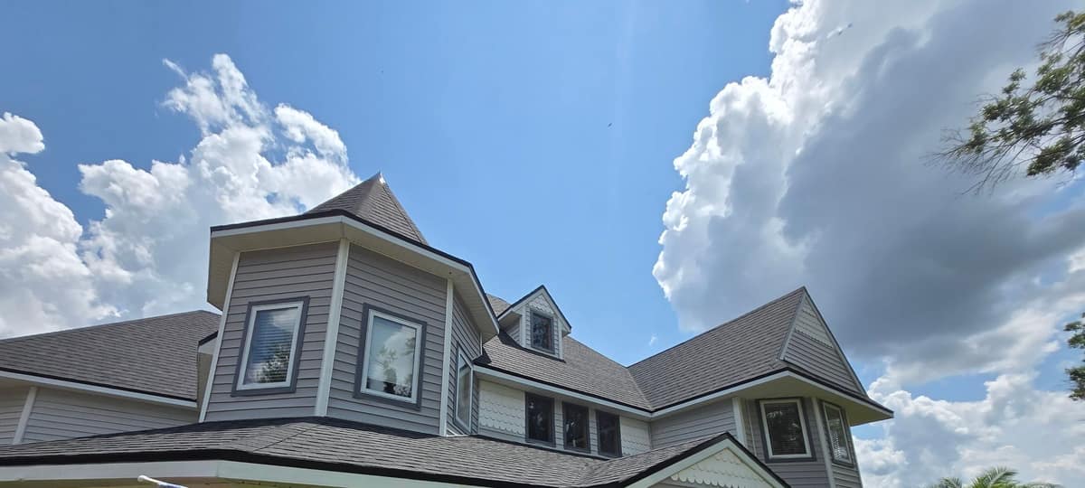 Turret cone, dormer and hip roofs in new Black Shadow shingles on a Clermont home under summer clouds