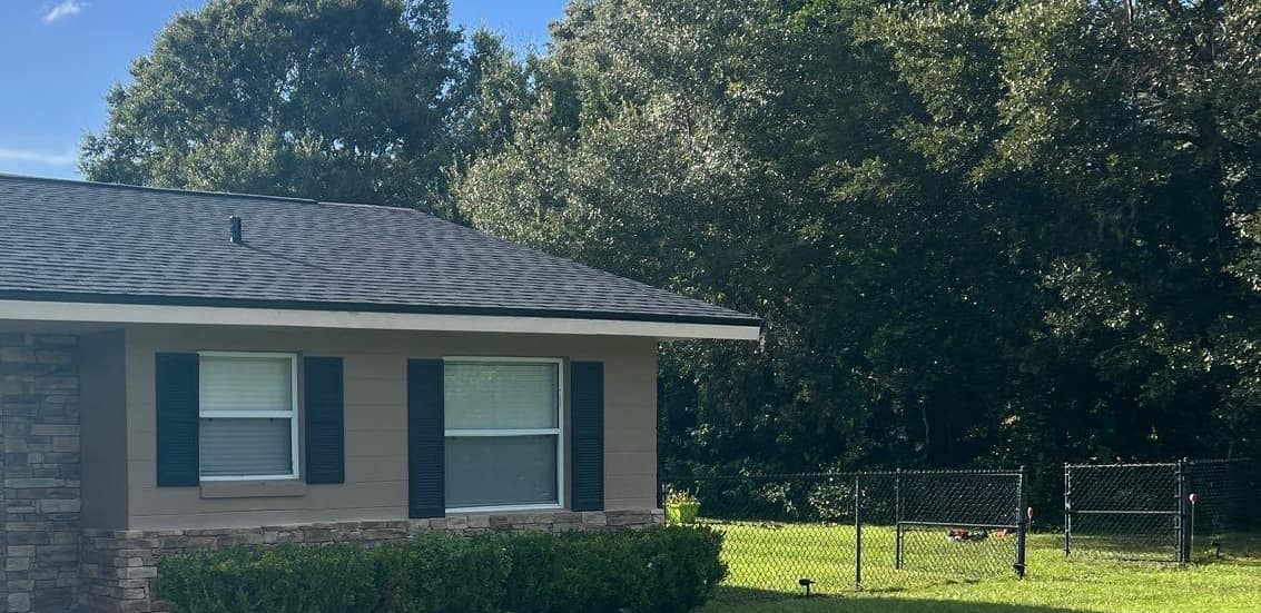Front wing of a DeLand ranch with tan siding, a stone base and a new Rustic Black roof