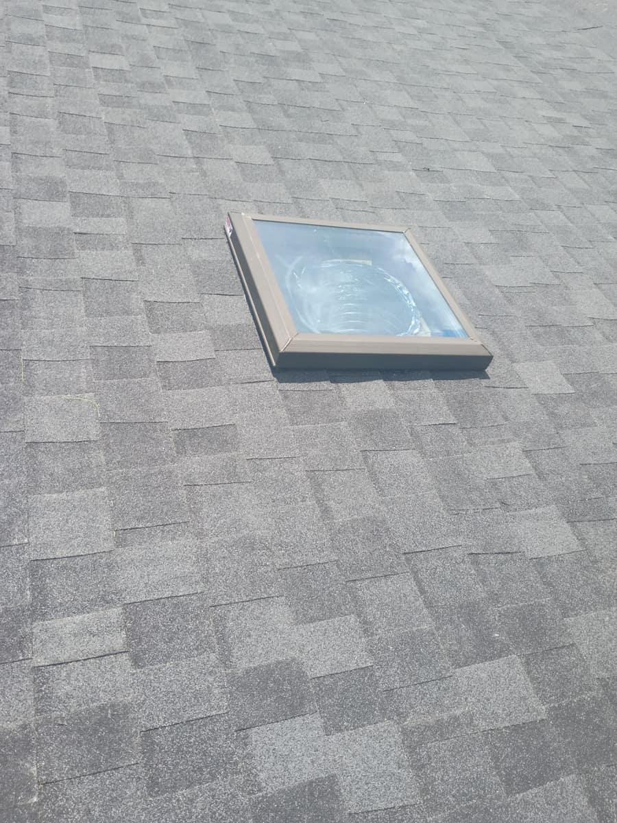 Close view of a skylight in a tan metal frame, with shingle courses fitted on every side