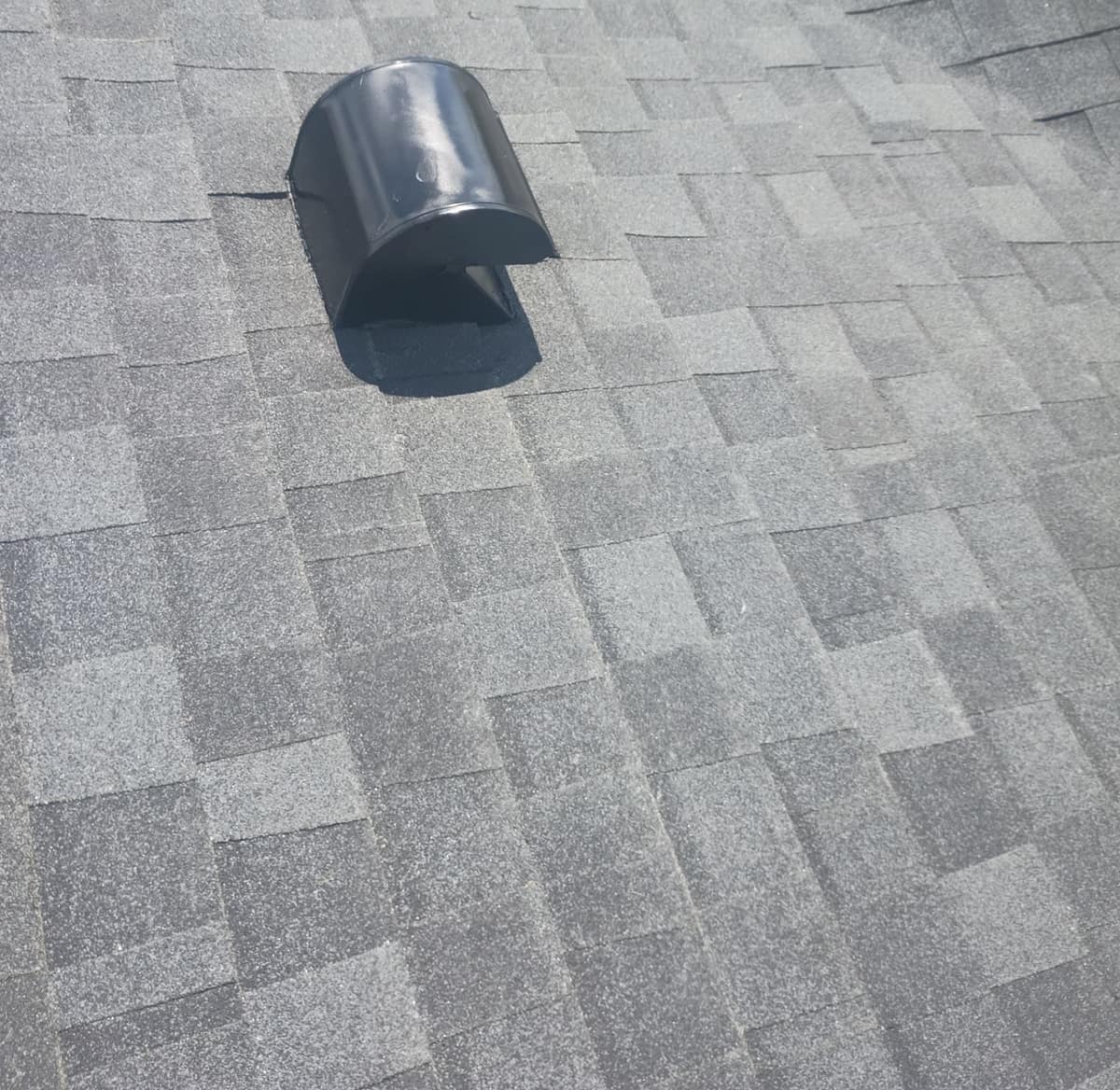 Black hood vent with a rounded cap set into the charcoal and slate shingle courses