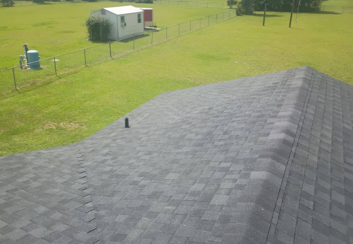 Hip caps on the new roof above a wide fenced field with a white shed and blue tank
