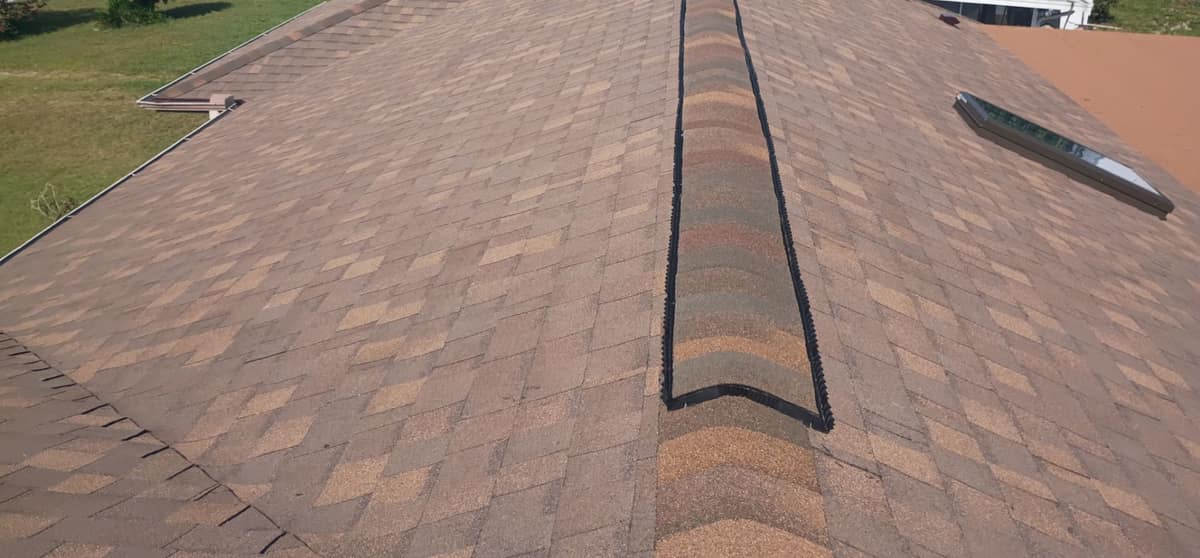 Ridge vent under capped ridge shingles on a Deltona roof, with a skylight on the right slope