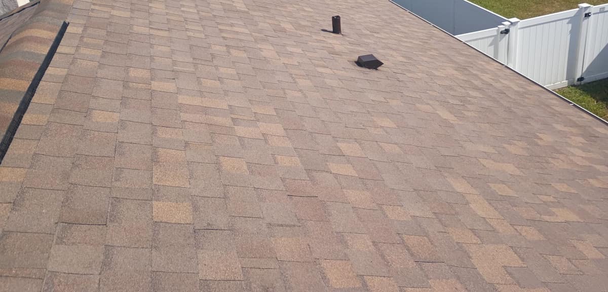 Back slope with a pipe vent and a brown box vent above a white vinyl fence