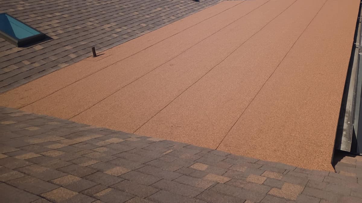 Low-slope section covered in copper orange cap sheet beside a shingled slope and a skylight