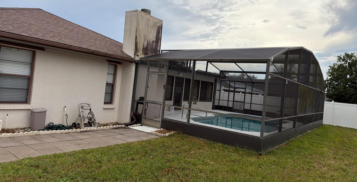 Back of the Deltona ranch with the new roof, a stucco chimney and a screened pool