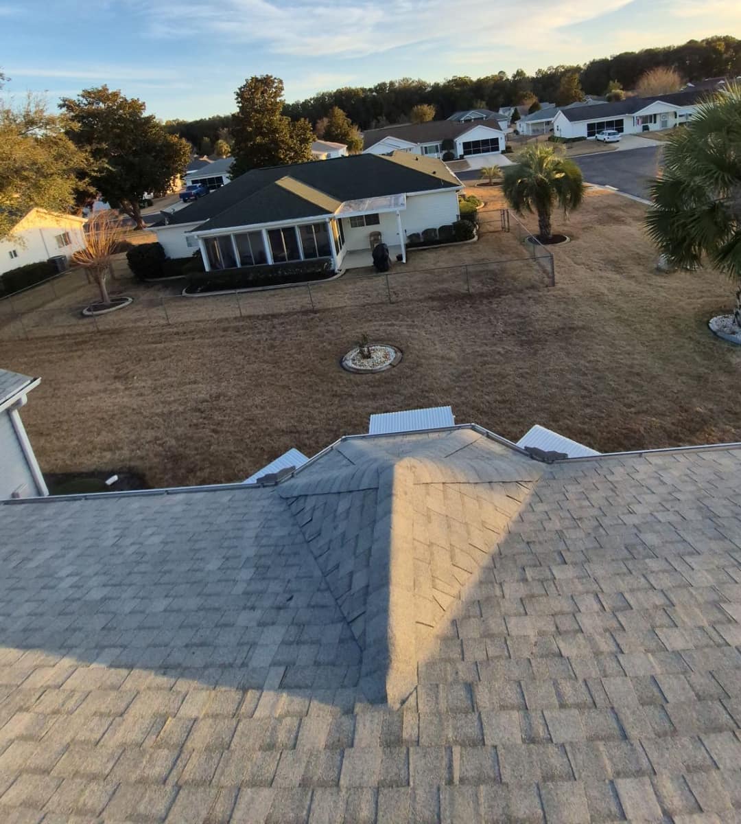 Looking over a hip on the new roof toward a fenced yard and a screened porch