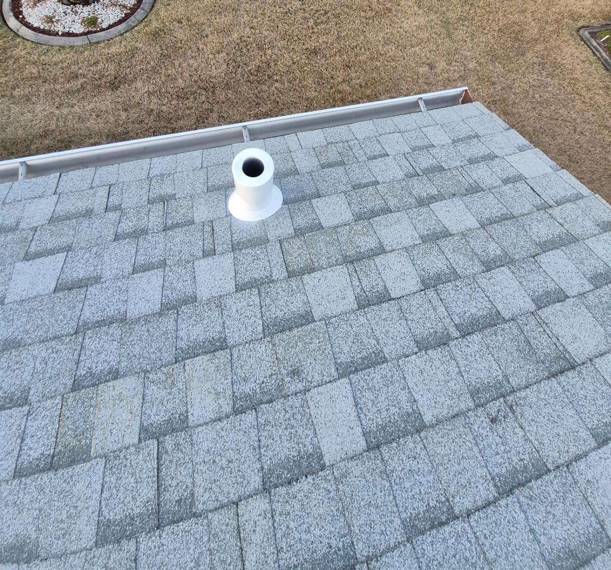 Close view of a white pipe vent flange and the aluminum gutter at the roof edge in Dunnellon