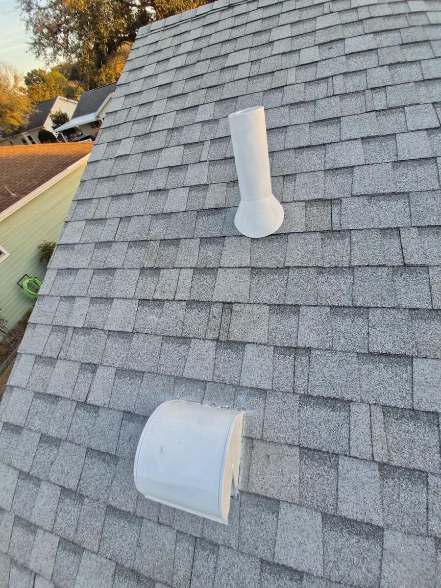 Close view of a tapered white pipe vent and a white gooseneck vent on the gray shingle slope