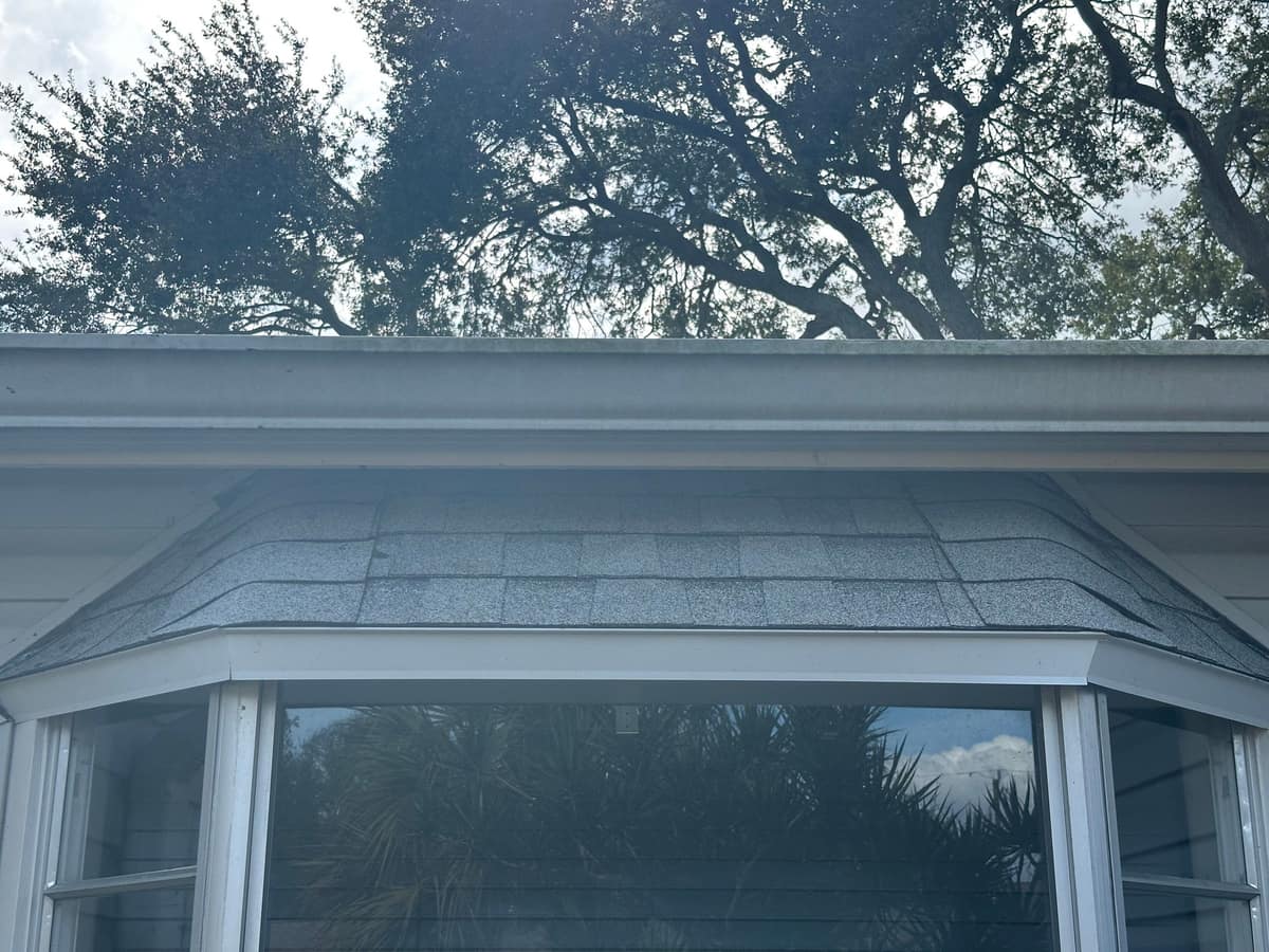 New shingles curving over the small roof above a bay window, under a white gutter