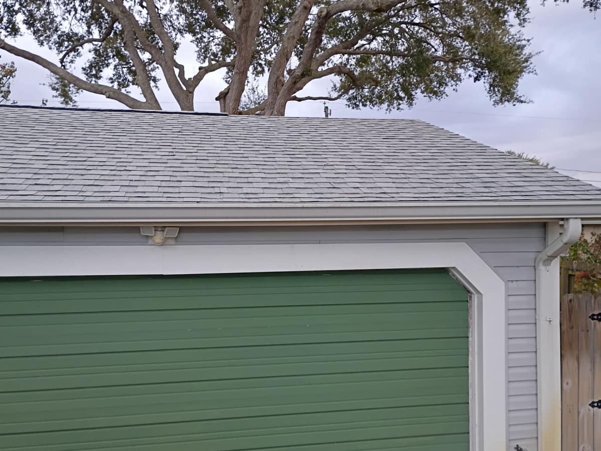 Garage roof edge with a white gutter and downspout above a green garage door