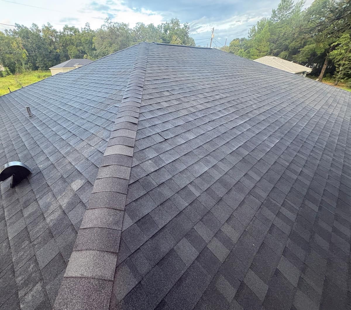 Rustic Black shingles on an Ocala hip roof with a curved exhaust vent and tall oaks behind