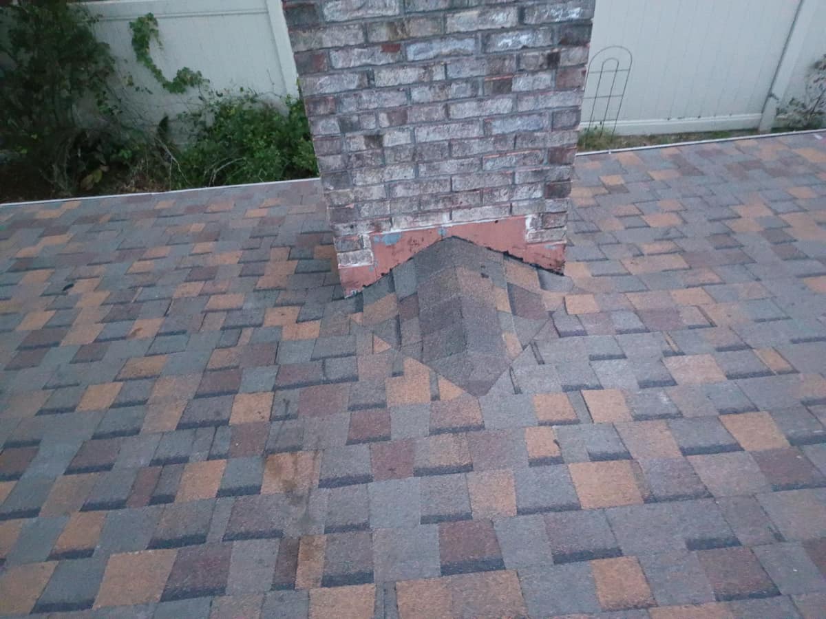 Small shingled cricket on the uphill side of the brick chimney, reddish flashing at its base