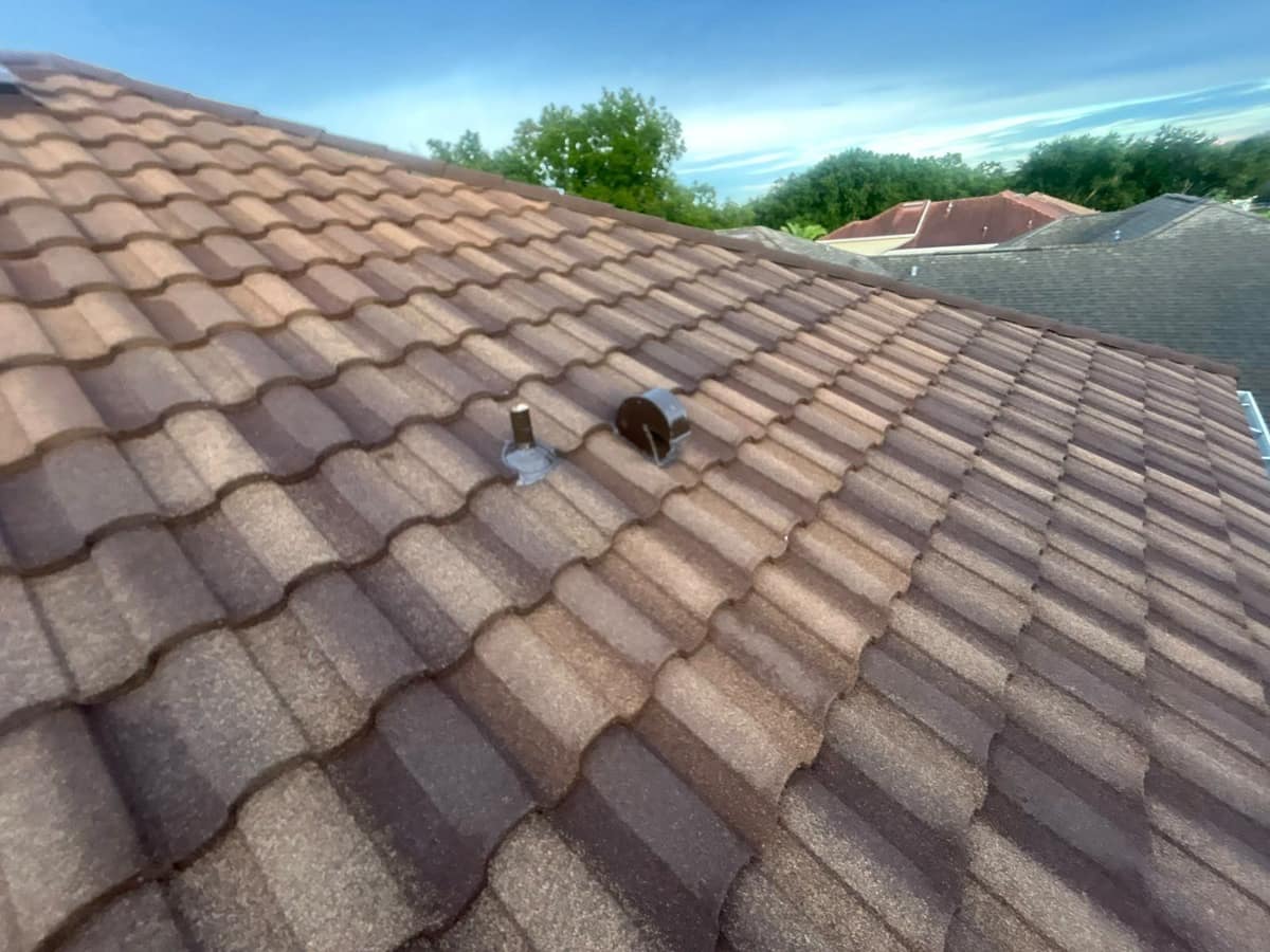 Pipe vent in a gray flashing collar beside a round hooded exhaust vent on the tile