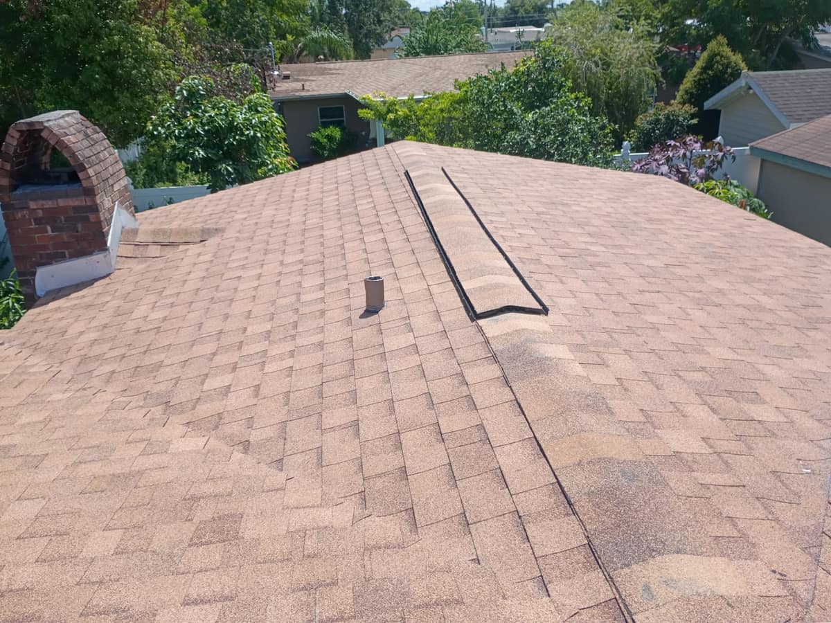 Ridge vent under tan cap shingles beside a pipe vent and the arched brick chimney