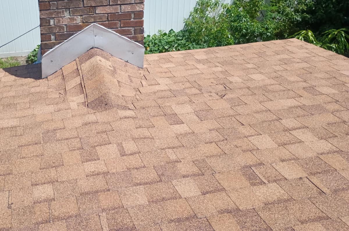 Bright metal flashing bent to a peak where a capped hip meets the brick chimney