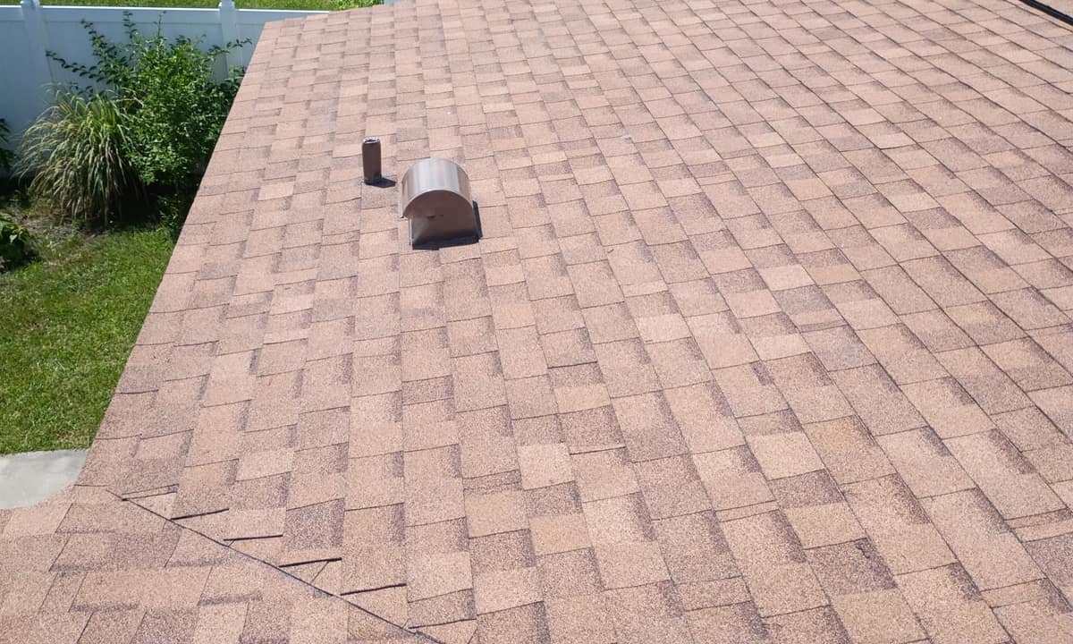 Curved hood vent and slim pipe vent on a tan slope above the fenced side yard