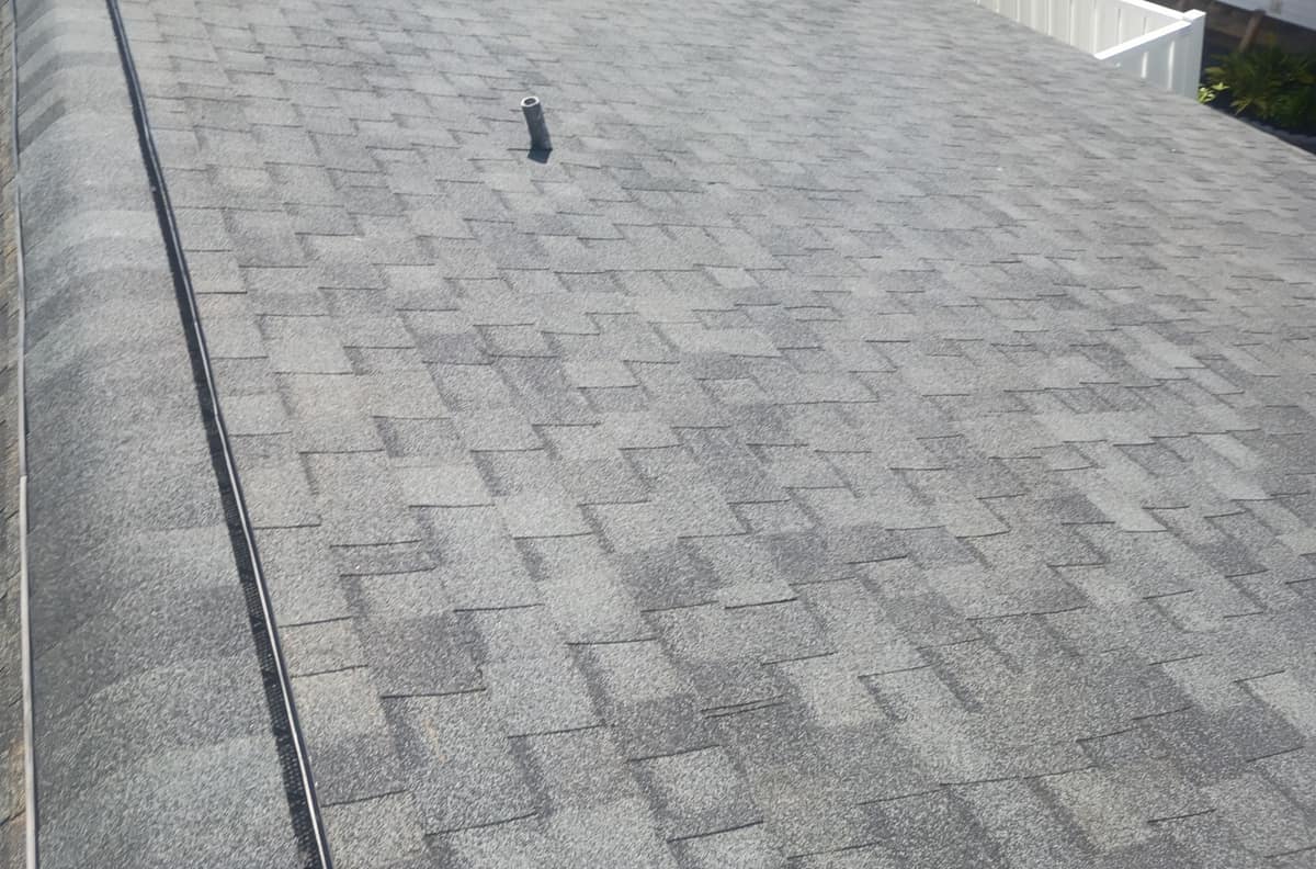 Close view of the ridge vent's black mesh edge beside the cap shingles, with a pipe vent