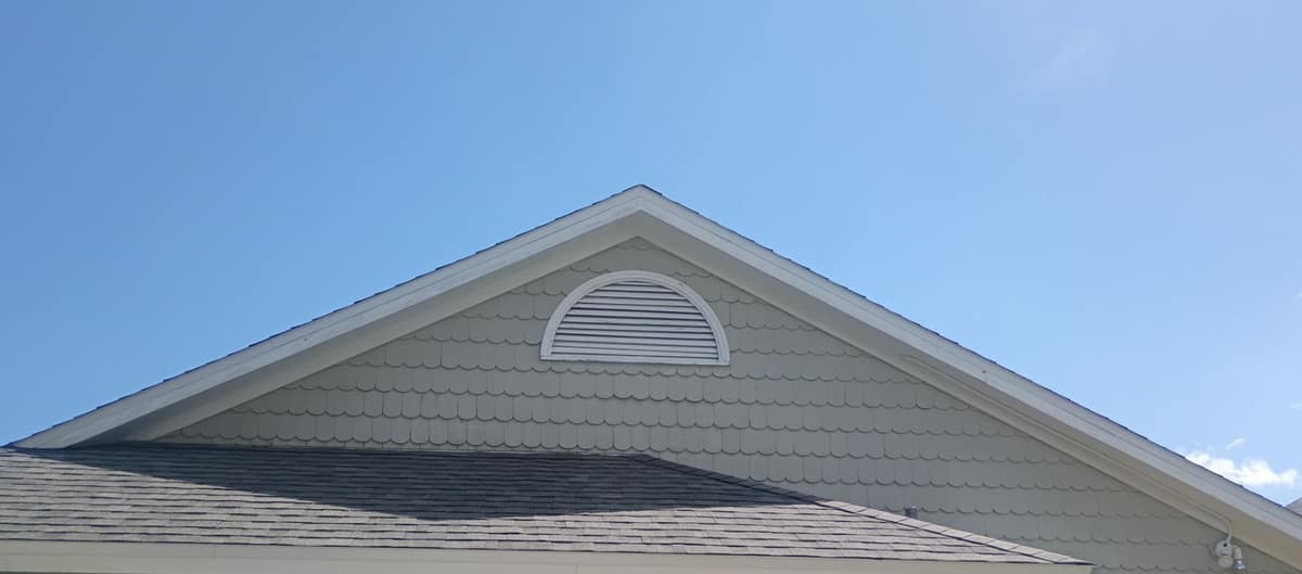 Front gable in pale gray scalloped siding with a half-round vent above the new garage roof